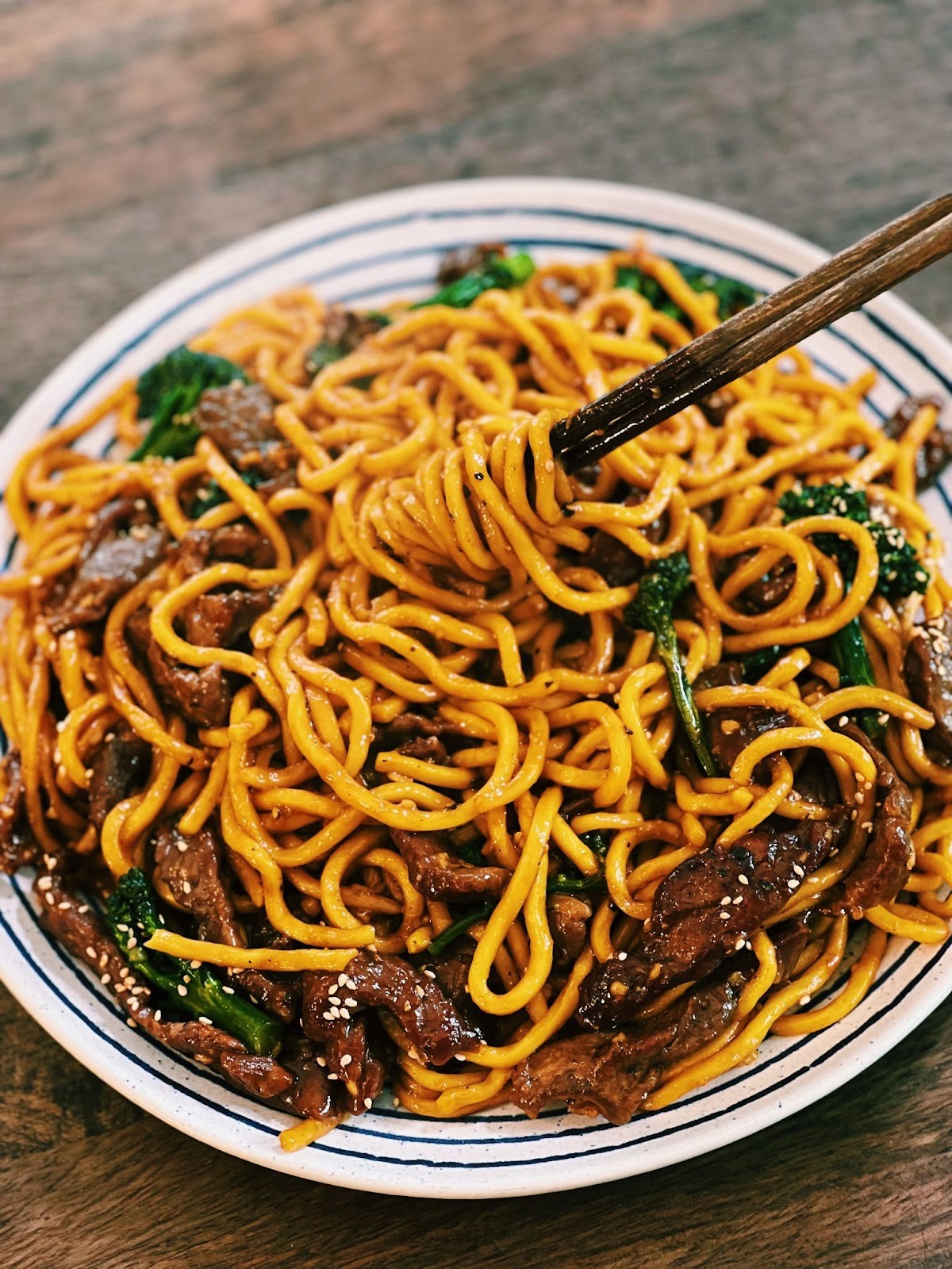 Beef Broccoli Noodles on a plate on a wooden table, with chopsticks.